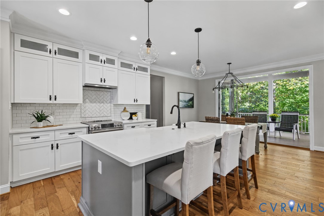 Kitchen featuring white shaker-style cabinetry with glass-front uppers, a central island with a contrasting base and solid-surface countertop, white subway tile backsplash in a herringbone pattern, wood-finish flooring, and pendant lighting