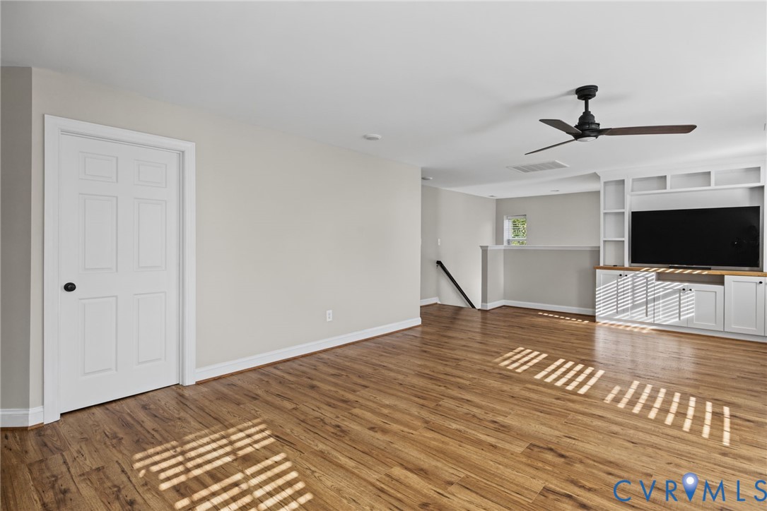 Interior space featuring wood-finish flooring, white built-in cabinetry, and a ceiling fan with matte black finish