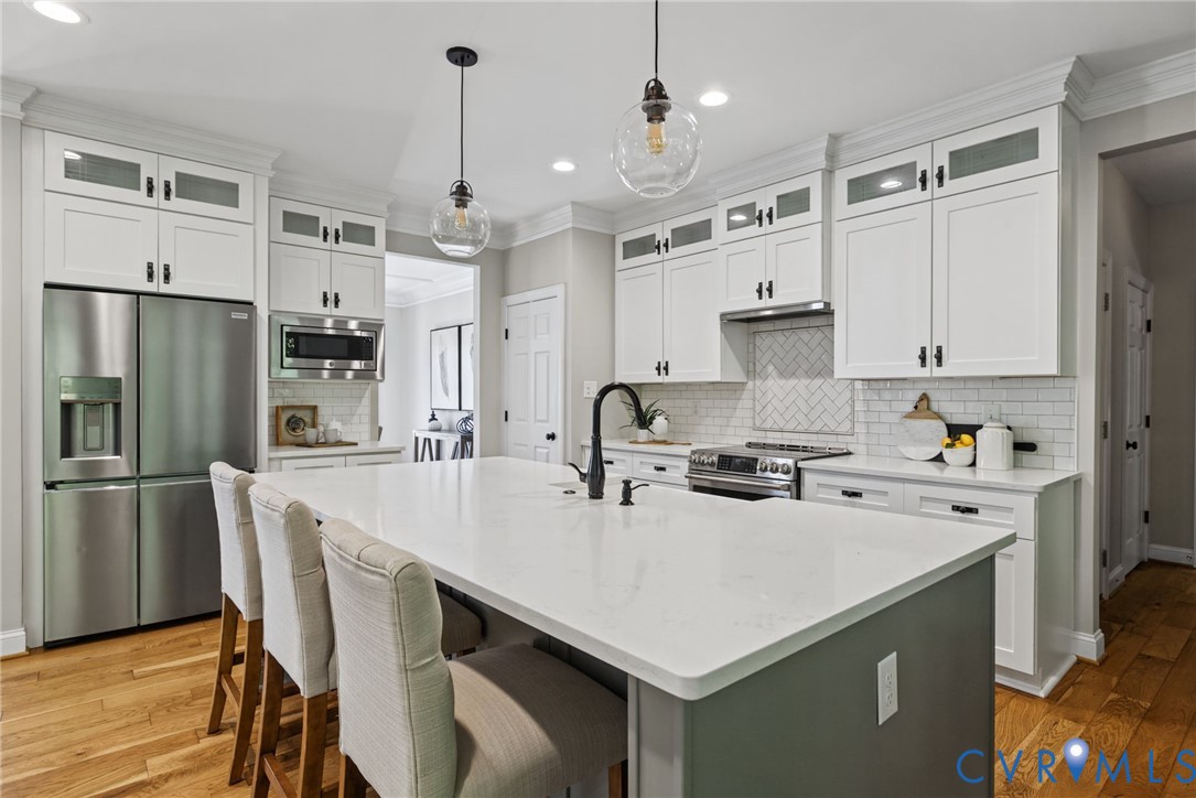 Kitchen featuring white cabinetry with glass-front uppers, a central island with a quartz countertop, stainless steel appliances, herringbone-pattern tile backsplash, and wood-finish flooring