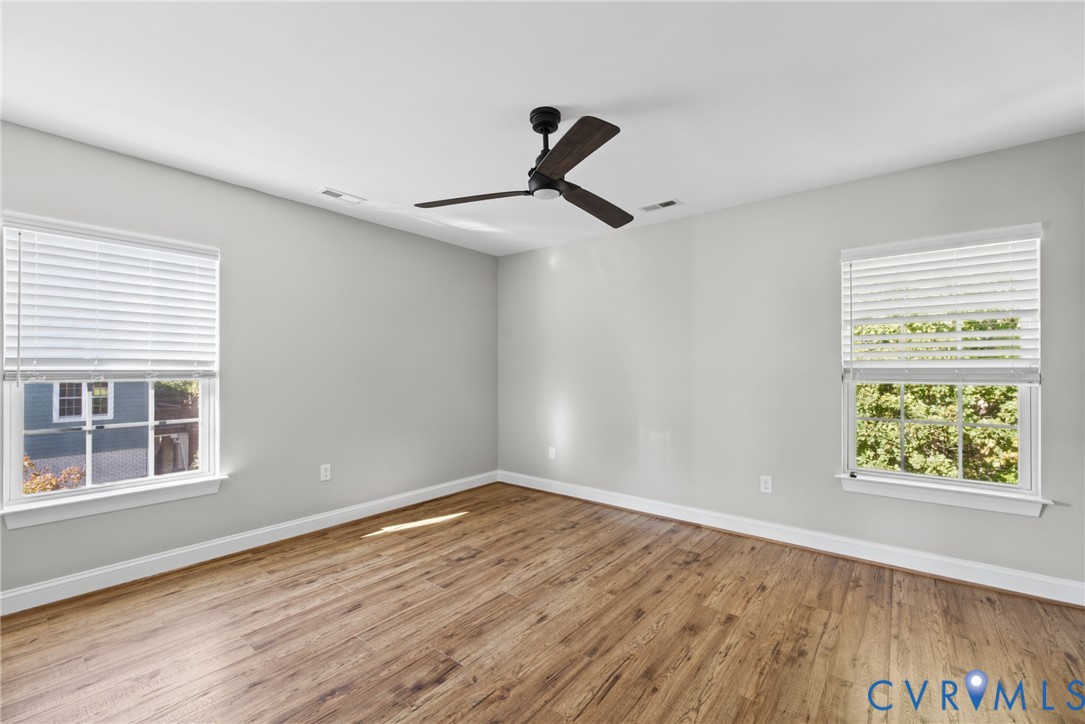 Room featuring wood-finish flooring, a matte black three-blade ceiling fan, and windows with integrated blinds