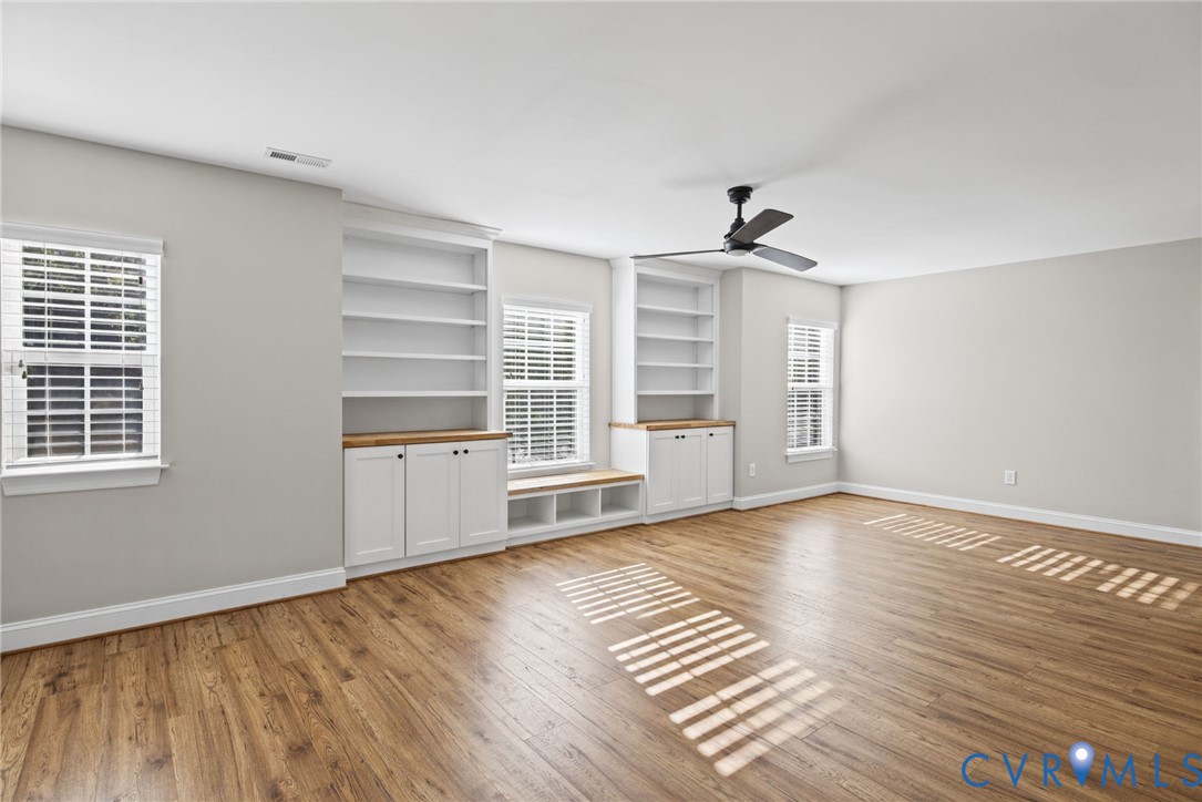 Wood-finish flooring, built-in shelving with lower cabinetry, integrated bench seating, multi-pane windows with white frames, and a ceiling-mounted fan