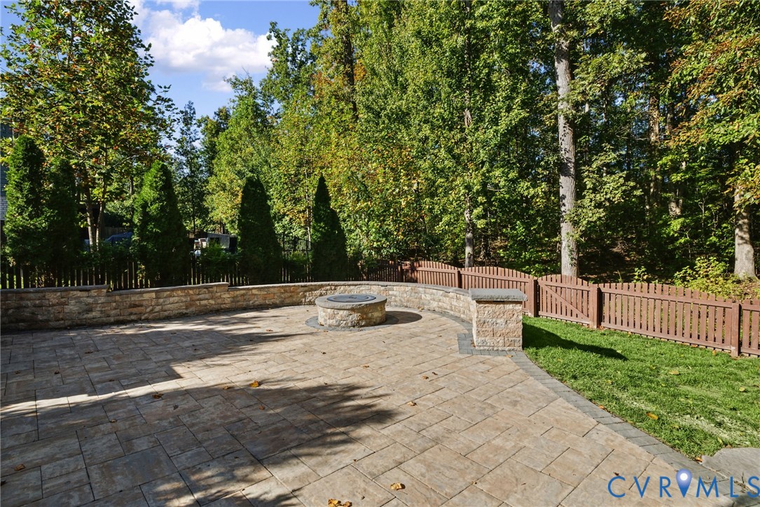 Paver patio featuring a built-in stone fire pit, tiered stone retaining wall, and wooden perimeter fencing