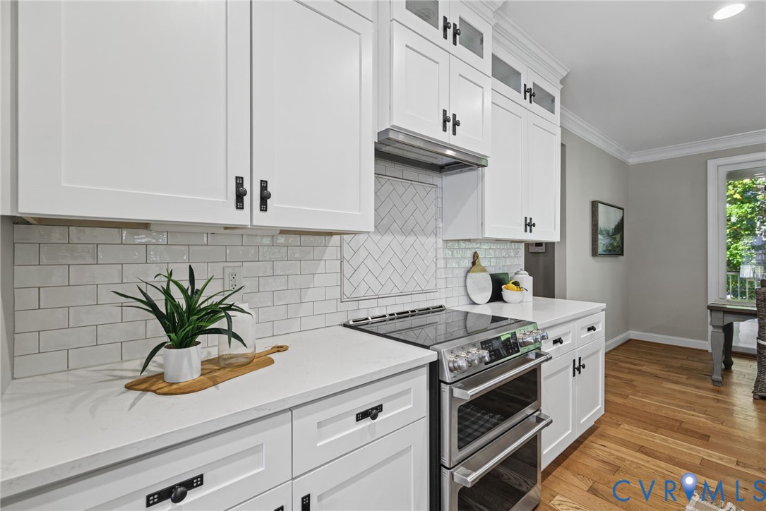 Kitchen featuring white Shaker-style cabinetry, quartz countertops, subway tile backsplash with herringbone detailing, stainless steel double oven, and wood-finish flooring