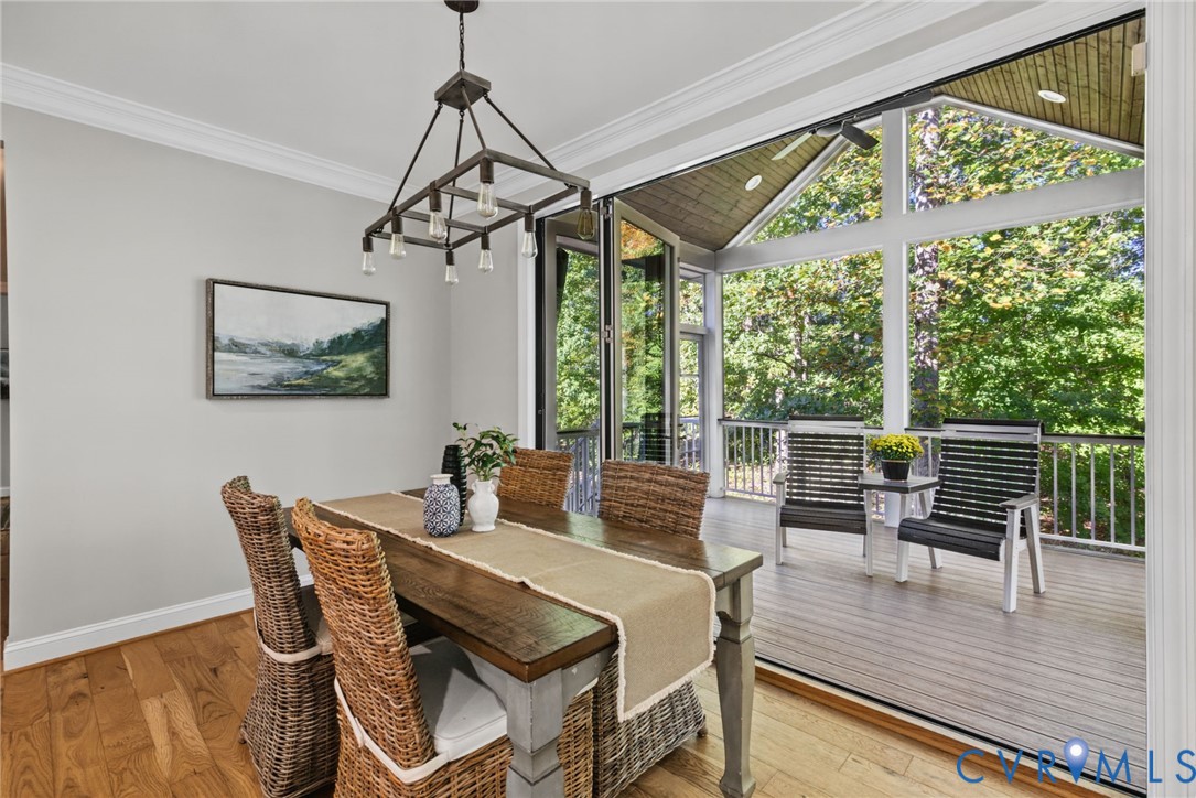 Dining area featuring wood-finish flooring, crown molding, a multi-light industrial chandelier, and floor-to-ceiling bi-fold glass doors opening to a covered deck with wood-finish decking and a peaked tongue-and-groove ceiling