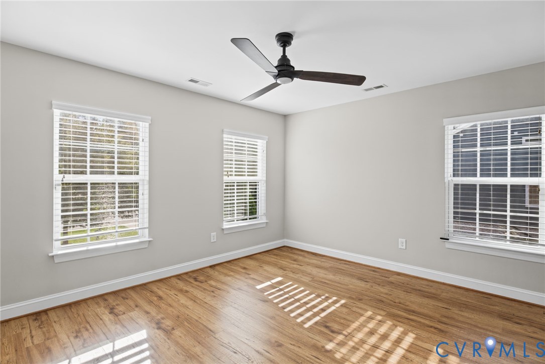 Room featuring wood-finish flooring, three windows with horizontal blinds, and a matte black ceiling fan