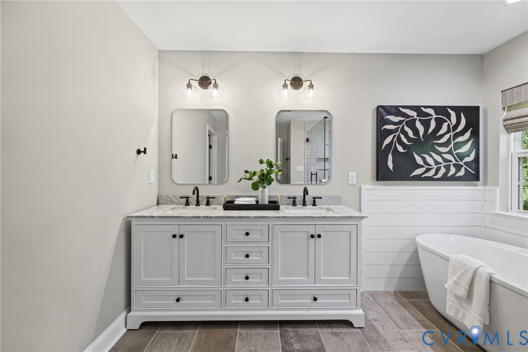 Double vanity featuring a stone countertop, dual undermount sinks with matte black faucets, rectangular wall-mounted mirrors, two-tone cabinetry, and a freestanding soaking tub with shiplap wainscoting