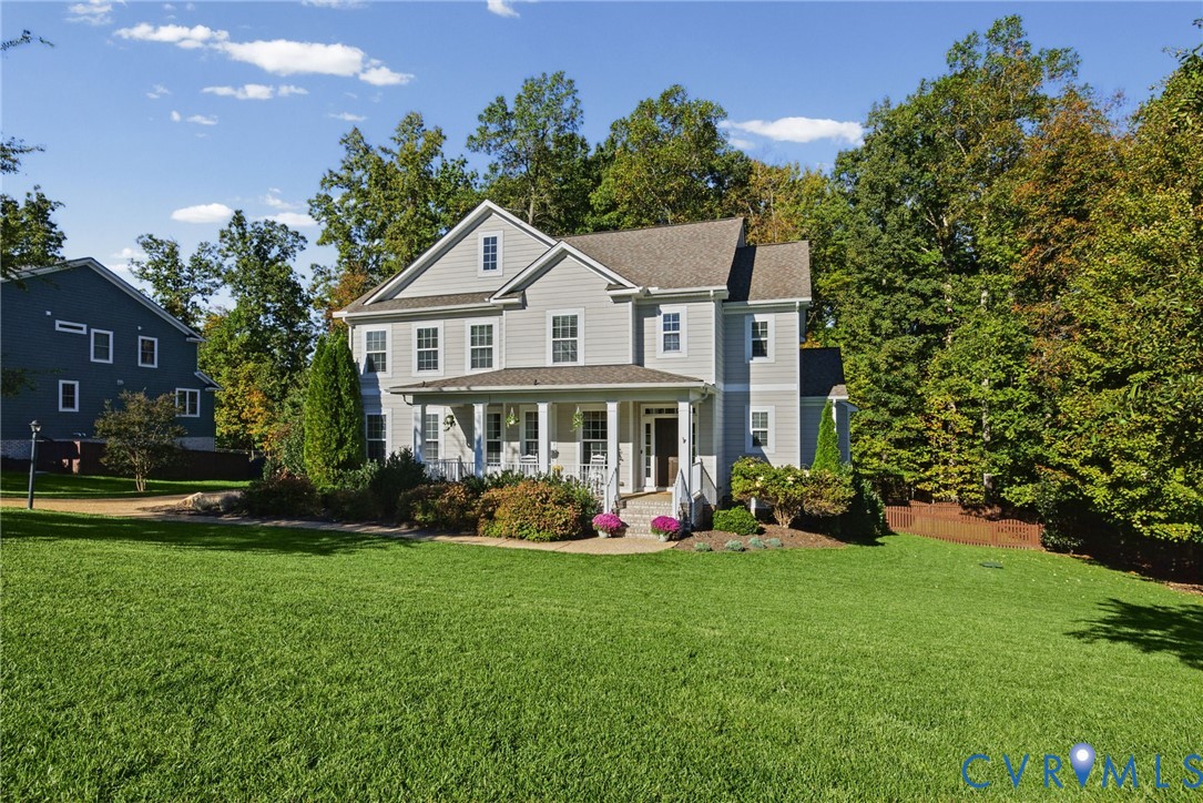 Two-story home with light-toned horizontal siding, a covered front porch featuring square columns, a gabled roofline, and extensive landscaped grounds