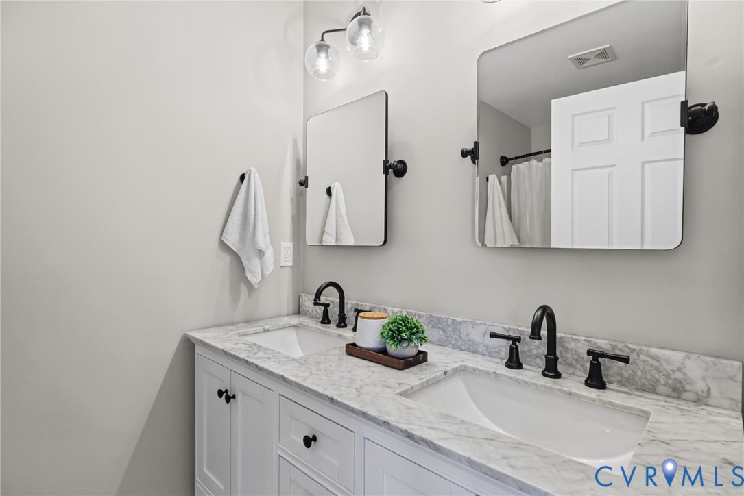 Dual-sink vanity with stone countertop, white shaker-style cabinetry, matte black widespread faucets, and twin rectangular mirrors with rounded corners