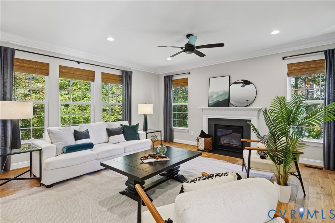 Living area featuring wood-finish flooring, crown molding, recessed lighting, a ceiling fan, and a fireplace with a decorative mantel