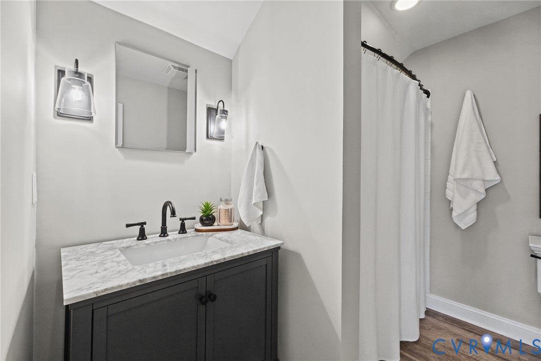 Bathroom vanity featuring a dark-finish cabinet, stone-patterned countertop, integrated basin, and matte black widespread faucet fixtures complemented by dual wall-mounted sconces