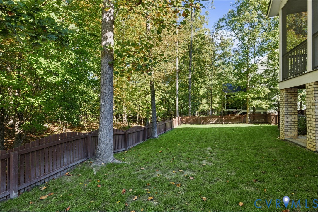 Backyard featuring a fenced lawn, mature trees, and a covered porch with brick foundation pillars