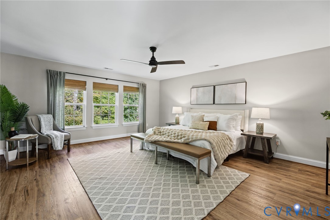Spacious room featuring wood-finish flooring, a matte black ceiling fan, and triple windows with integrated wooden blinds