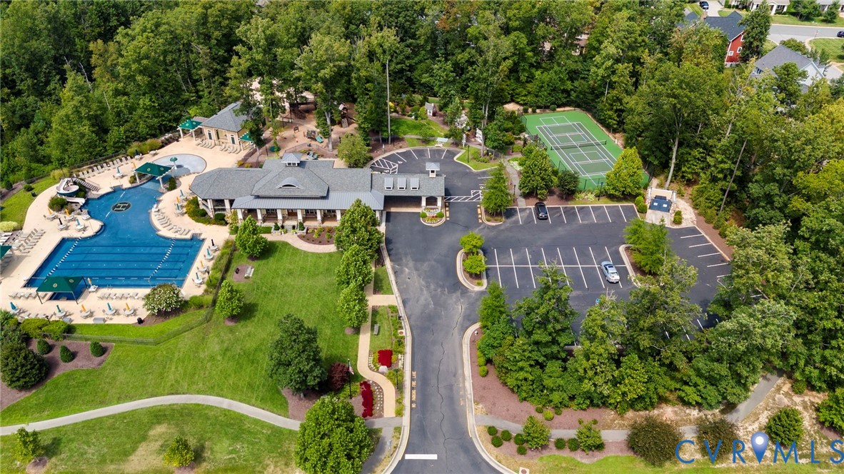 Community recreation complex featuring an outdoor swimming pool, tennis court, clubhouse, paved parking area, and landscaped grounds