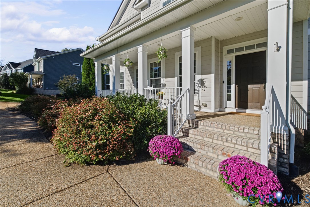 Covered front porch featuring white structural columns, a brick-tread staircase, horizontal lap siding, and multi-pane transom windows above the entryway