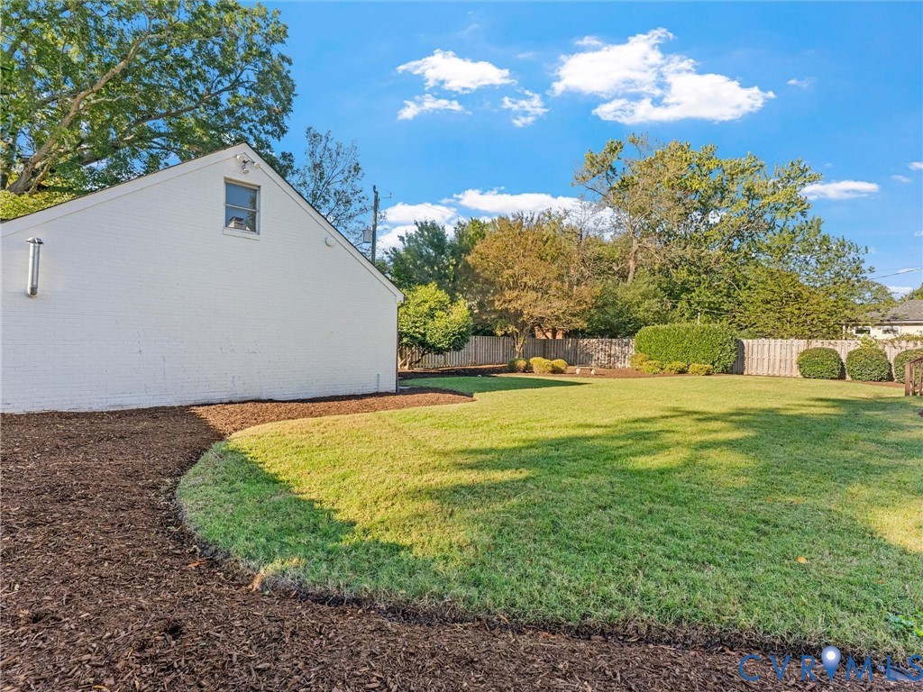 Expansive backyard featuring a manicured lawn, established landscaping, perimeter fencing, and a white-painted brick exterior