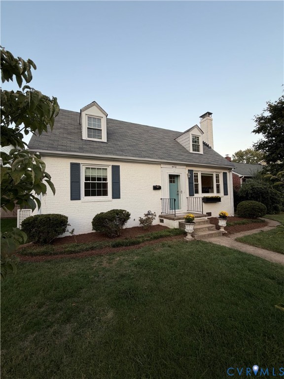 Painted brick exterior featuring dormer windows, decorative shutters, a masonry chimney, and a front entry with metal railings