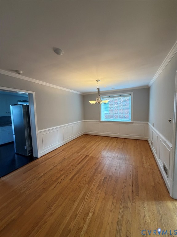 Interior space featuring wood-finish flooring, white wainscoting, crown molding, and a central multi-light chandelier