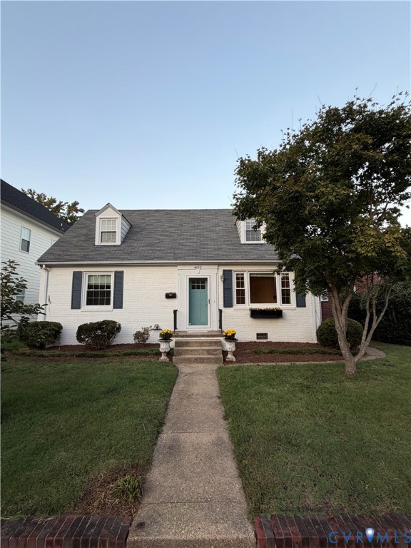 Cape Cod exterior featuring a painted brick facade, two dormer windows, shuttered multi-pane windows, and a concrete walkway