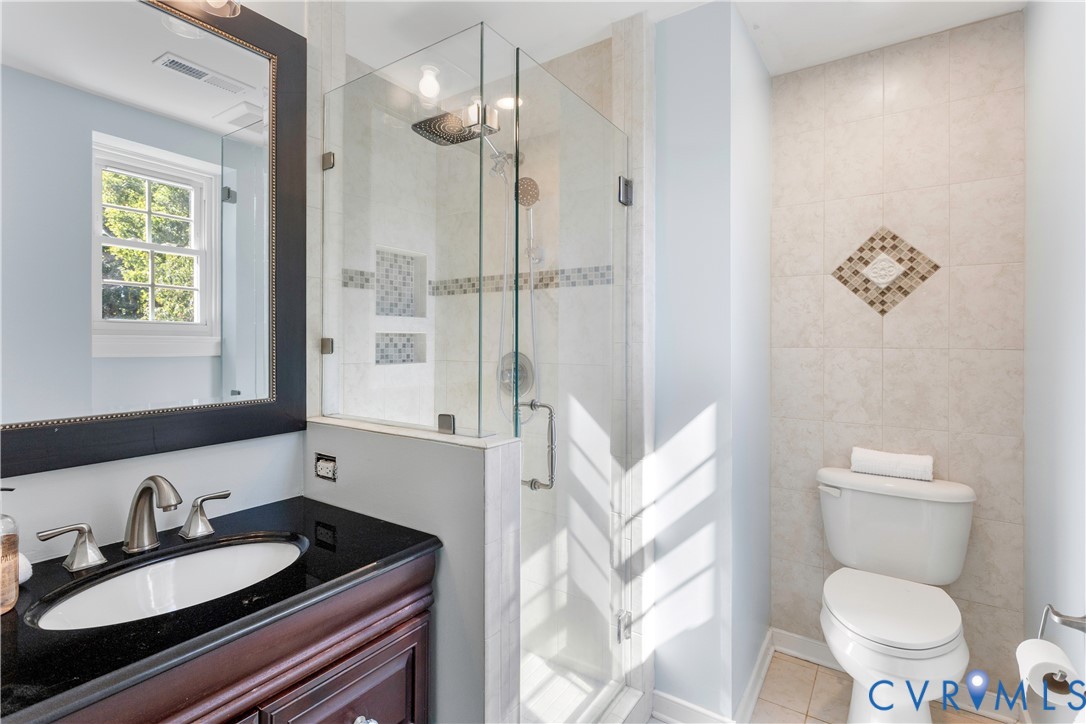 Bathroom featuring a dark wood-finish vanity, integrated oval sink with metal faucet, frameless glass enclosed shower with recessed shelving, and tiled wall accents
