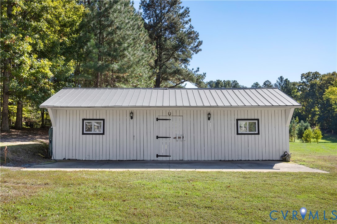 Detached outbuilding featuring vertical board siding, a standing-seam metal roof, two exterior wall-mounted lanterns, and double-entry doors with heavy-duty strap hinges