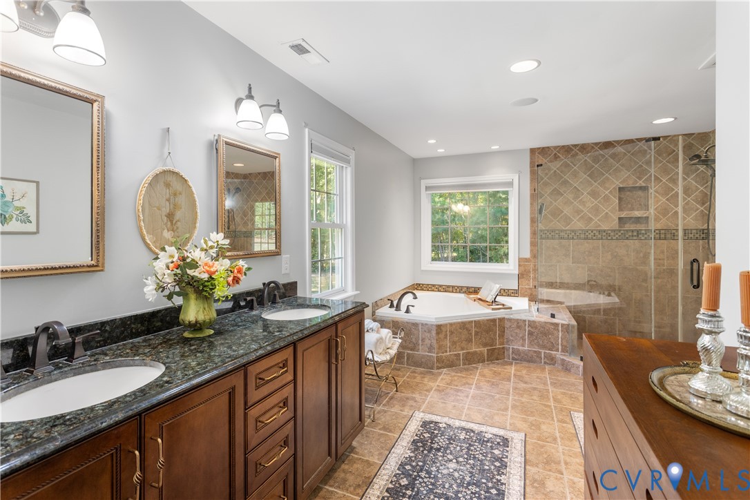 Dual-sink vanity granite countertops, wood-finish cabinetry, recessed lighting, corner jetted tub, and a tiled walk-in shower with a glass enclosure private water closet.