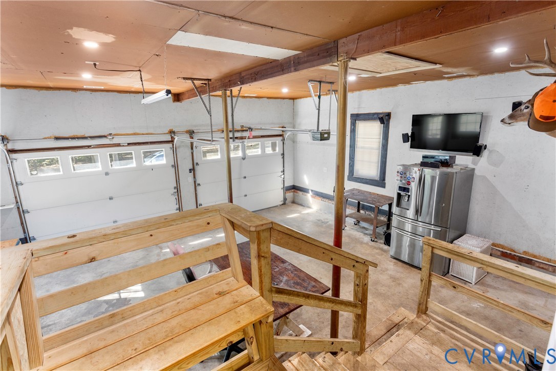 Multi-bay garage featuring overhead doors with glass panel inserts, recessed lighting, exposed structural ceiling beams, and integrated wood staircase railings