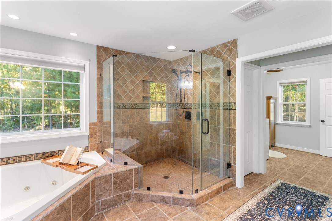 Walk-in glass-enclosed shower with diagonal wall tile, integrated recessed shelving, multi-head shower fixture, corner jetted tub, and ceramic tile flooring. adjacent laundrey room, walkin closet