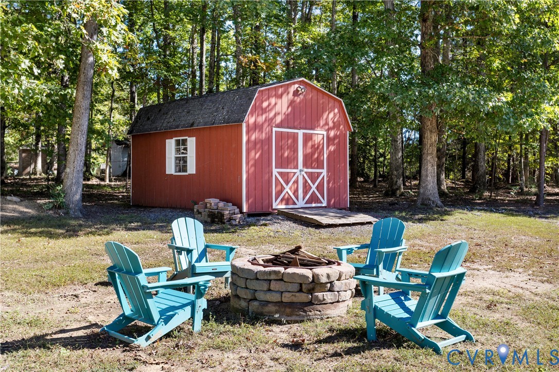 Barn-style storage structure featuring double doors, white trim accents, and a ramp, complemented by a circular stone-block fire pit