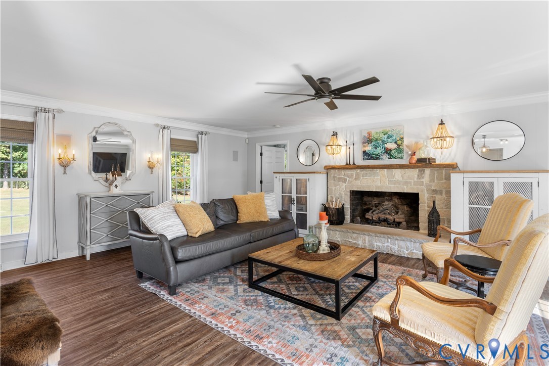 Stone fireplace with a wooden mantel, wood-finish flooring, built-in cabinetry, crown molding, and ceiling fan