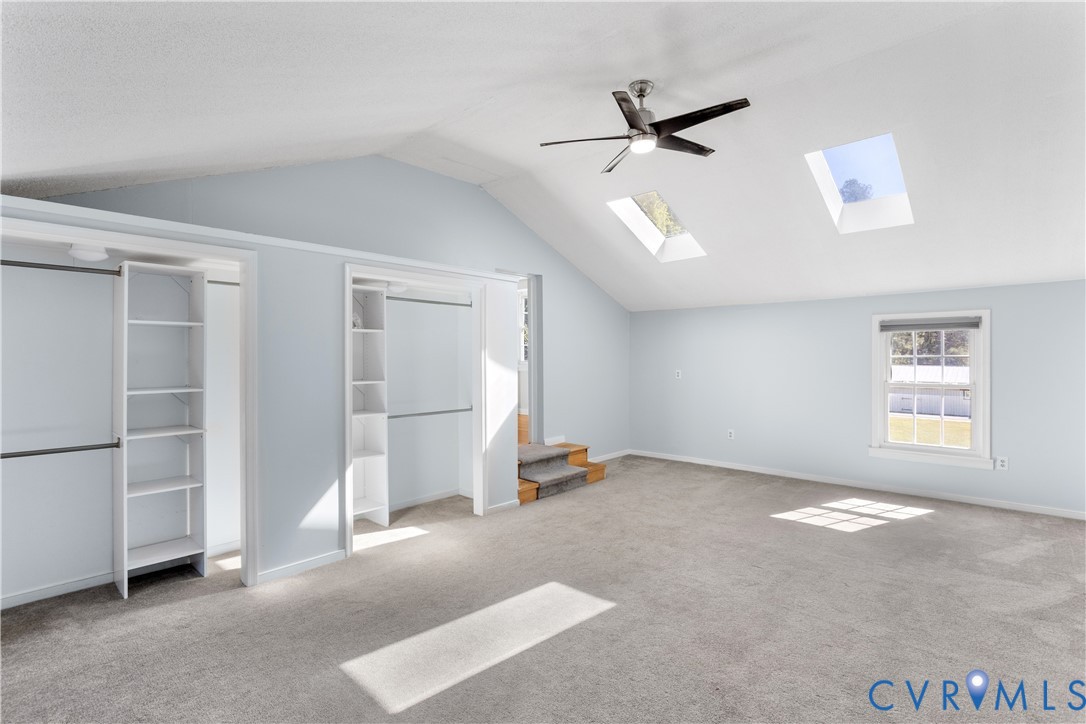 Vaulted ceilings featuring two skylights, a center ceiling fan, dual built-in closets with integrated shelving, and wall-to-wall carpeting