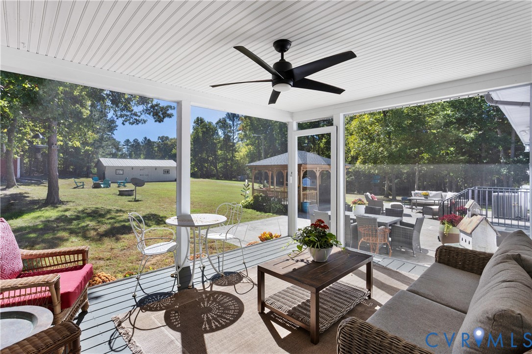 Screened-in porch featuring a beadboard ceiling, a matte black ceiling fan, and painted decking over looking the 1000 sq ft concrete patio / Outdoor entertainment courtyard. Wow a great view of the barn &  expansive yard!