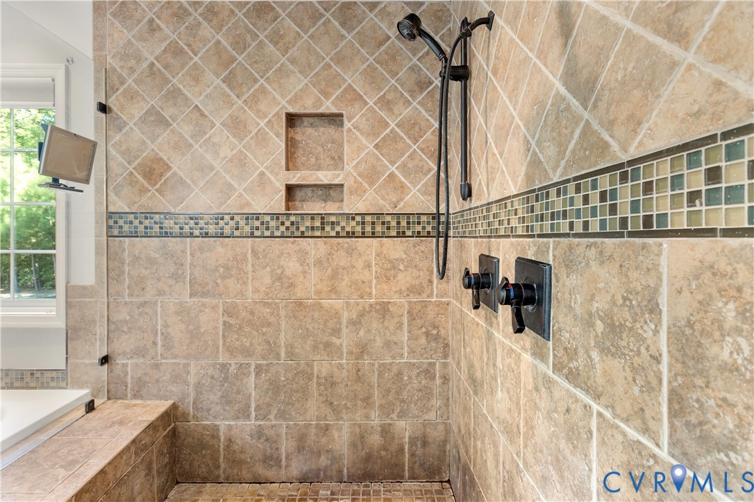 Walk-in shower featuring large-format stone-finish wall tile, decorative glass mosaic tile inlay, built-in recessed storage niche
