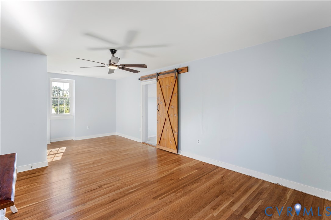 2nd floor primary  a sliding wood barn door, and a ceiling-mounted fan with integrated lighting. New refinished hardwood flooring! attached full bath. Adjoining multipurpose carpeted room HUGE!