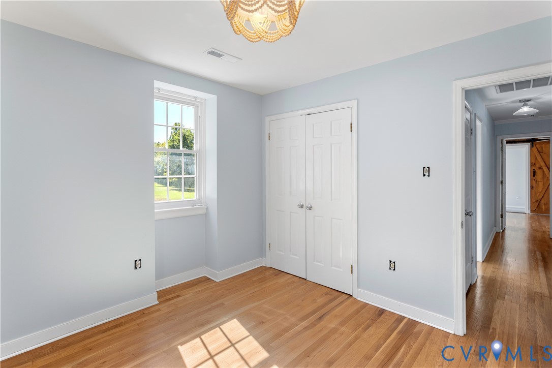 Room with wood-finish flooring, double-door closet, multi-pane window, and decorative pendant light fixture