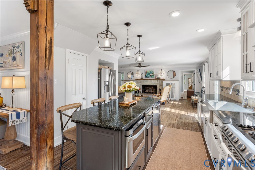 Kitchen featuring a center island with granitw countertops, white cabinetry, rustic wood support column, stainless steel appliances, and geometric pendant lighting