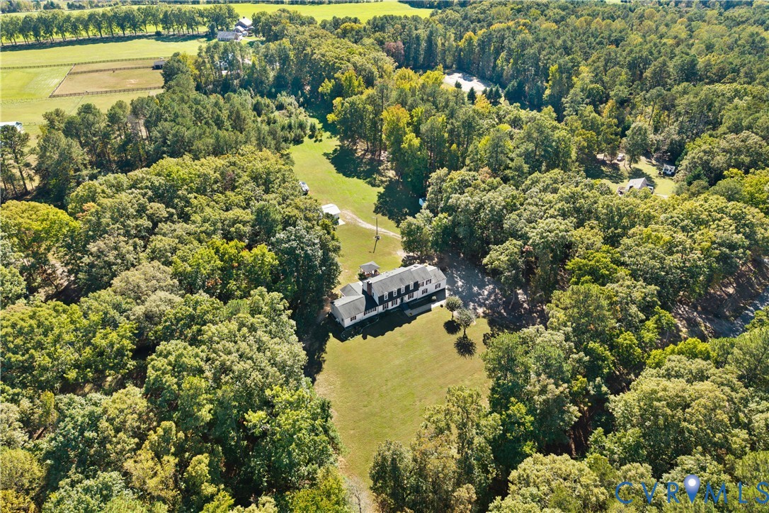Aerial perspective of a multi-story residence situated on a wooded lot featuring expansive grass clearings and a private driveway