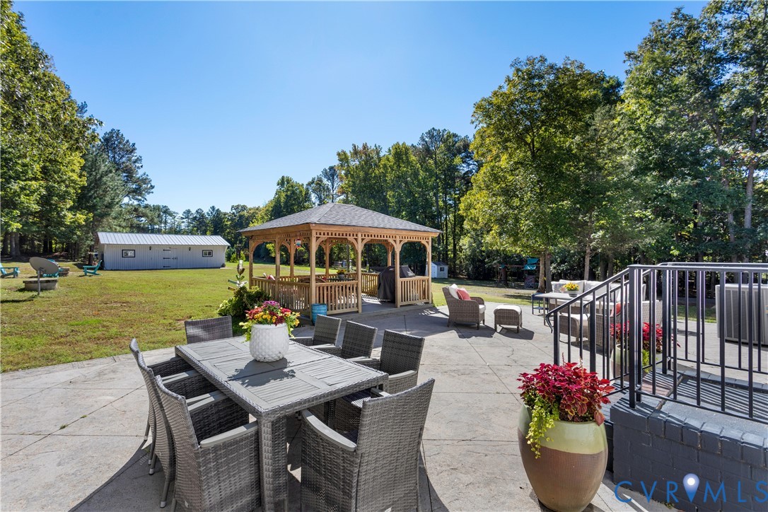 Expansive backyard featuring a concrete patio, a wooden gazebo, mature trees, and a detached outbuilding