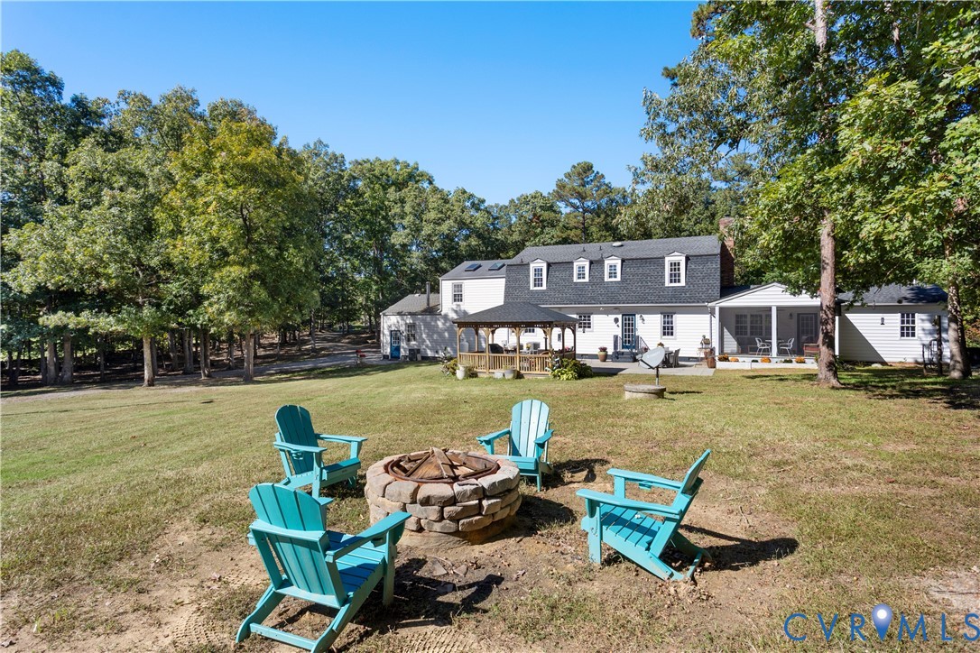 Expansive backyard featuring a stone fire pit, a covered gazebo, and a rear porch with mature trees