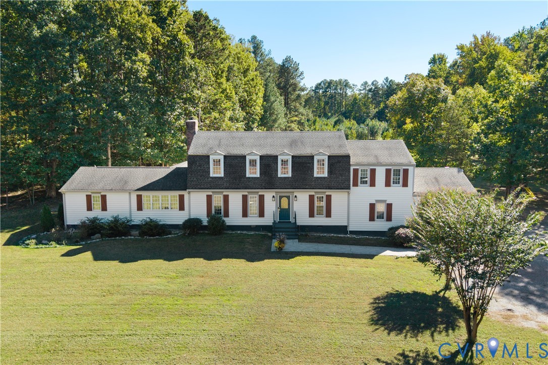 Two-story colonial-style residence featuring a gambrel roof, white siding, decorative window shutters, and a brick chimney, situated on a expansive lot with mature trees
