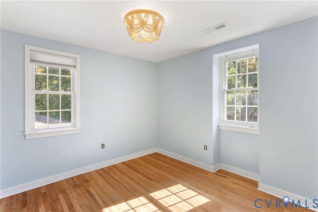 Room featuring wood-finish flooring, two double-hung windows with muntins, and a circular beaded-style flush mount light fixture