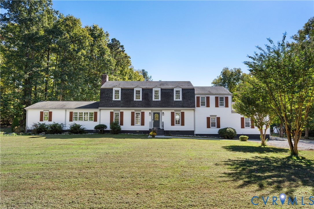 Colonial-style exterior featuring vinyl siding, a dark-toned mansard roof, symmetrical window placement, decorative shutters, and an expansive front lawn