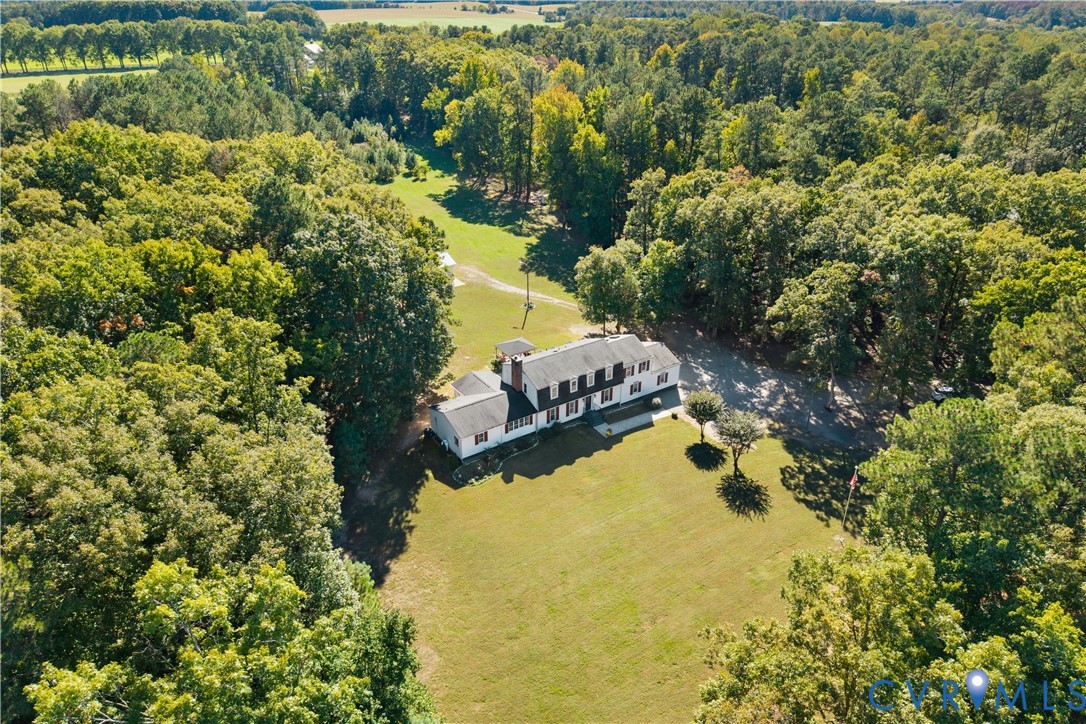 Multi-story residence featuring a shingled roof, exterior brick chimney, sprawling grounds, and extensive perimeter woodland