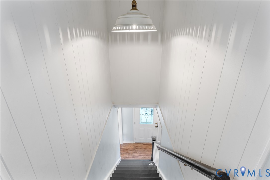Stairway featuring white vertical paneled walls, a metal dome pendant light, and a dark-toned handrail.