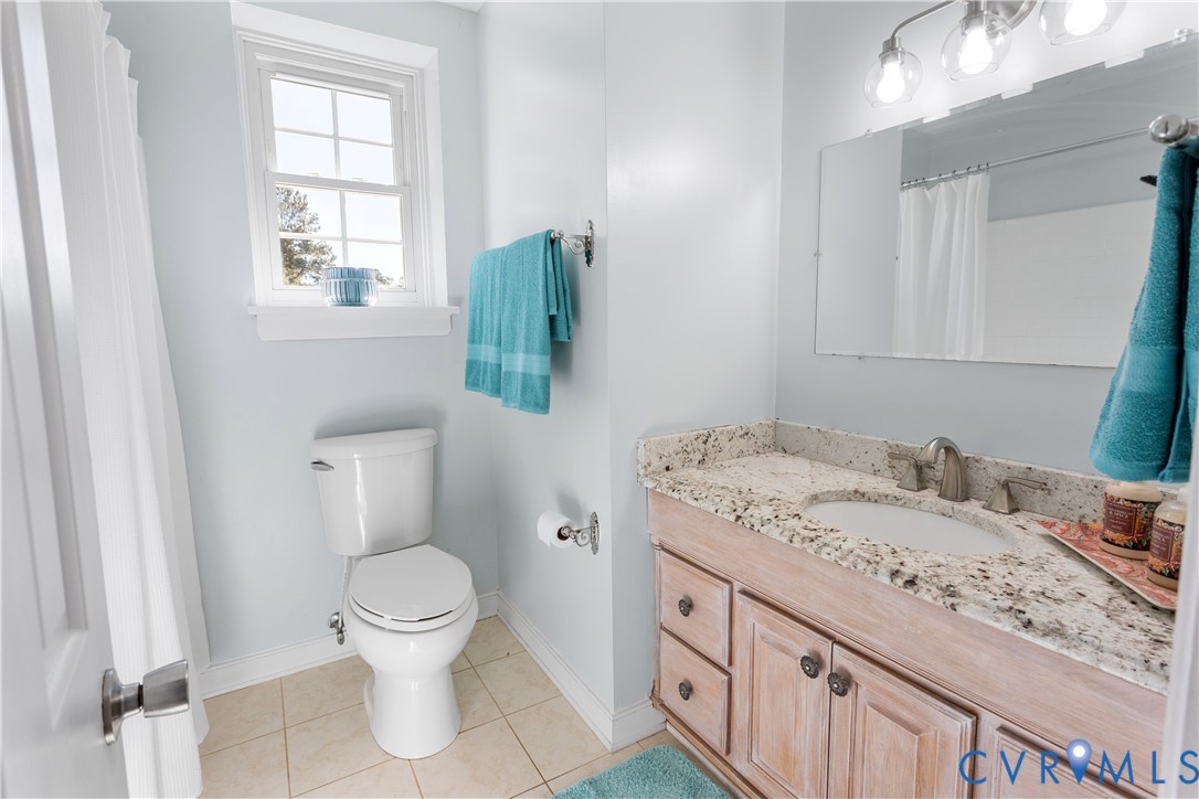 Bathroom featuring a vanity with stone-finish countertop, light wood-finish cabinetry, tile flooring, and a wall-mounted multi-bulb light fixture
