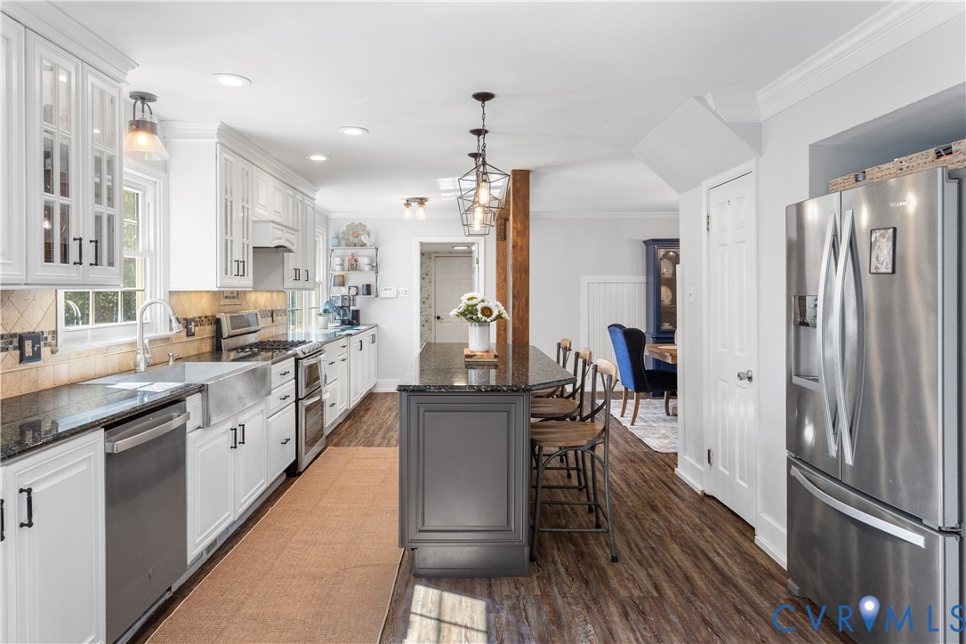 Kitchen featuring white cabinetry with glass-panel accents, stone-finish countertops, stainless steel farmhouse sink, center island with charcoal-finish base, and wood-finish flooring