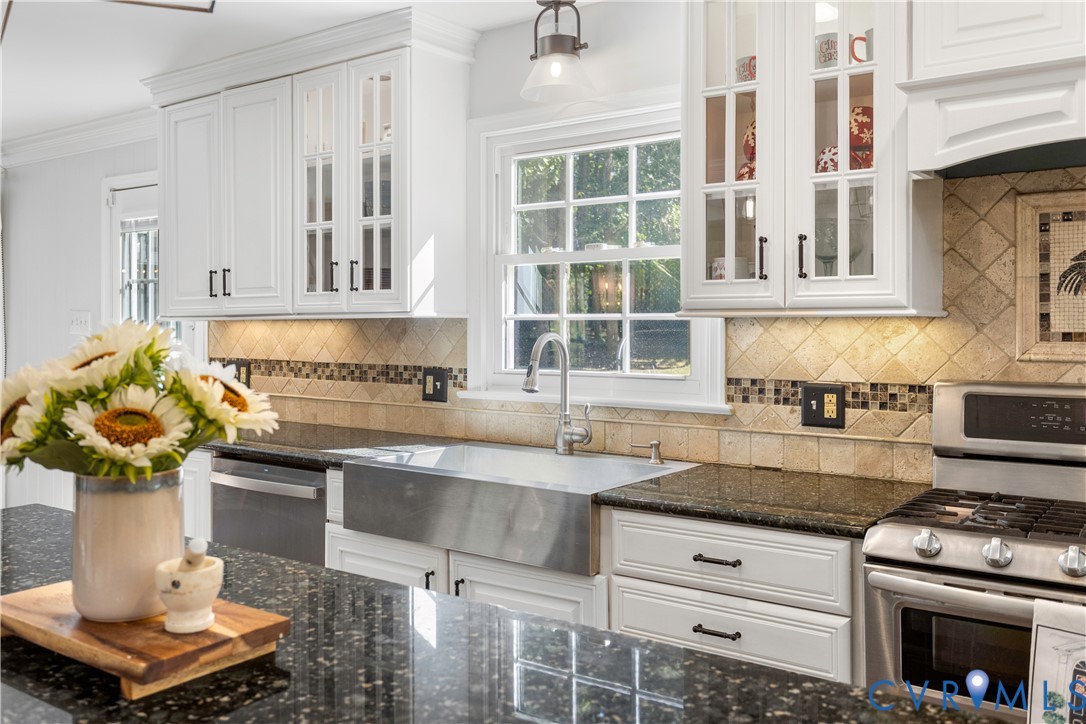 Kitchen featuring white cabinetry with glass-front uppers, granite countertops, stainless steel farmhouse sink. Window over the sink with perfect views of the year yard and gazabow