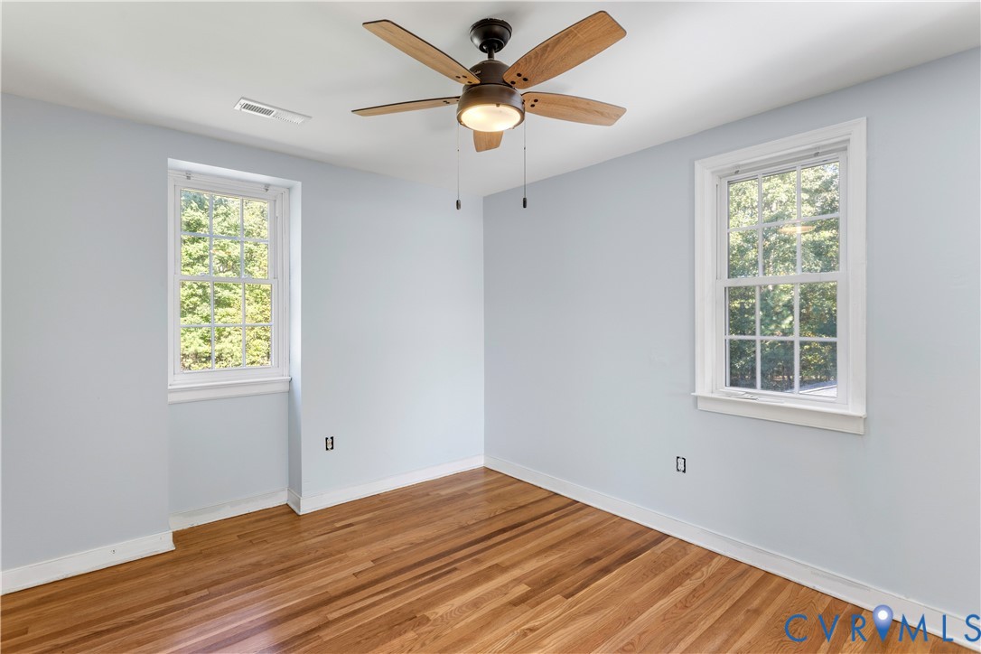 Room featuring wood-finish flooring, two multi-pane windows, and a ceiling fan with integrated lighting
