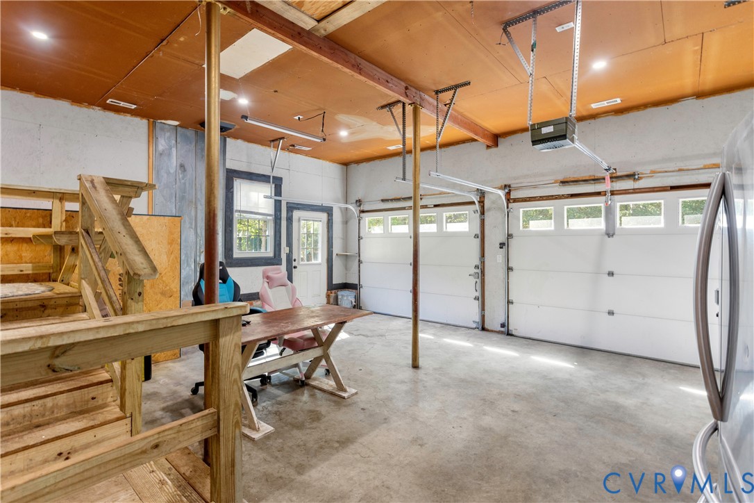 Attached garage featuring concrete flooring, dual overhead door systems, recessed ceiling lighting, and a wood-framed staircase