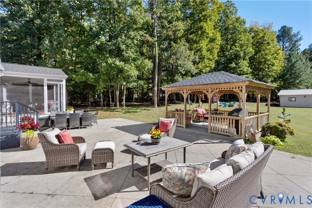 Spacious concrete patio featuring a wooden gazebo with a shingled roof, a covered porch, and mature surrounding woodland