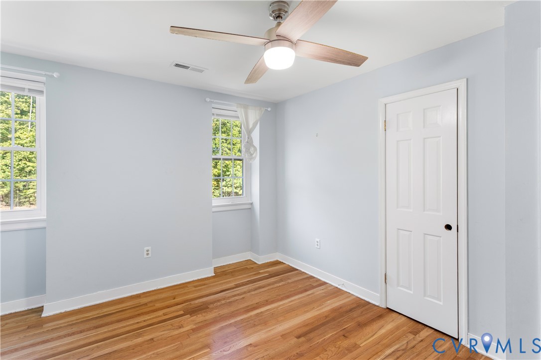 Room featuring wood-finish flooring, multi-pane windows, and a ceiling fan with integrated lighting